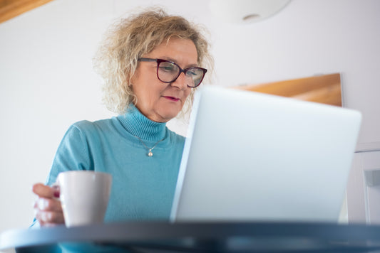 person med blå bluse og briller sidder med kaffekop og laptop